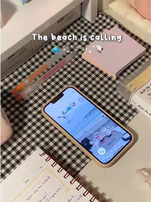 The image shows a phone displaying an app screen with a beach scene on a black and white checkered surface. There are stationary items like pens and notebooks on the table too.