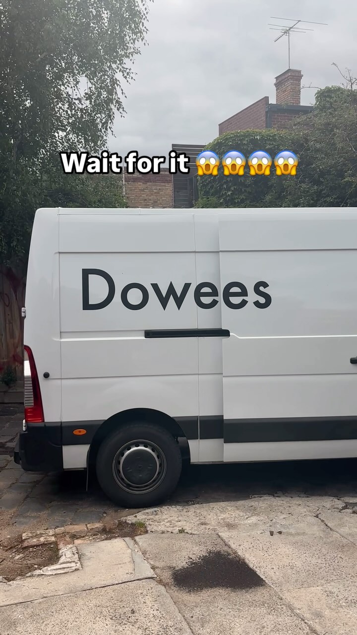 A white van is parked on a paved surface. The side of the van is visible, featuring large, black text that spells out a word. Above the van, the top half of buildings and trees are visible under a cloudy sky. A layer of white text with a black outline overlaid on the image reads 'Wait for it' along with four shocked face emojis.
