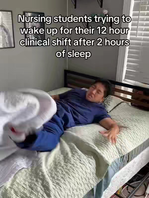 A person is lying in bed, looking disoriented and trying to wake up. The person is lying on their back with visible signs of having been asleep, such as messy hair and a sleepy expression. A blanket is pulled up as if the person is trying to get out of bed.