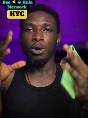 A man with dark skin and short, neatly-styled hair looks directly at the camera. He has a slight beard and is holding a green phone in his right hand. The man is wearing a black tank top. The background is a blurry purple gradient.  A text overlay at the top left of the image says Bee & Rubi Network KYC in a mix of black and yellow.