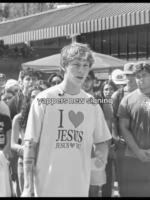 A black and white image of a young man speaking to a crowd. He is wearing a t-shirt that says 'I heart Jesus'. The text 'yappers new signing' is overlaid at the top of the image.