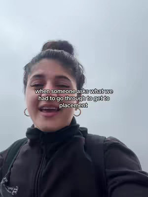 A young woman with dark hair pulled back is looking towards the camera and smiling. The background is an overcast, pale sky. The top of the woman’s black jacket is visible. There is text overlaid on the image in a sans serif font.