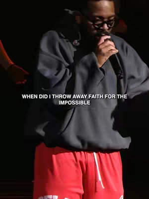 The cover image shows a man on stage, wearing a dark gray hoodie and red shorts. He's holding a microphone and singing, with dramatic, low lighting. The background is dark, likely a concert or studio setting, and text overlays are present.