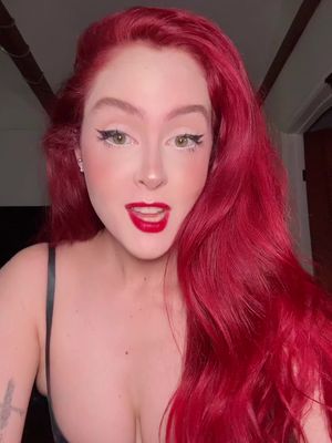 The video cover features a young woman with bright red hair looking directly at the camera. She has dramatic eye makeup and bold red lipstick. The lighting is bright and flattering, emphasizing her features. The background appears to be a softly lit indoor space.