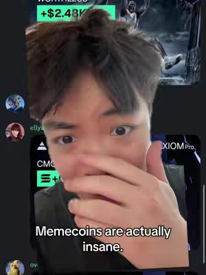 A selfie-style video cover image featuring a young man, his face taking up most of the frame. He has dark hair and is looking towards the camera with an expression of concern or slight surprise, his hand covering his mouth. Behind him, there are blurred elements of a phone screen displaying financial data, possibly a trading app. There are app icons and text overlays. At the bottom, a text overlay reads, 'Memecoins are actually insane.'