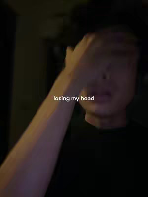 A person is holding their hand up to their forehead, slightly obscuring their face. The image is dark, with the person's face partially visible, and a text overlay says 'losing my head'.
