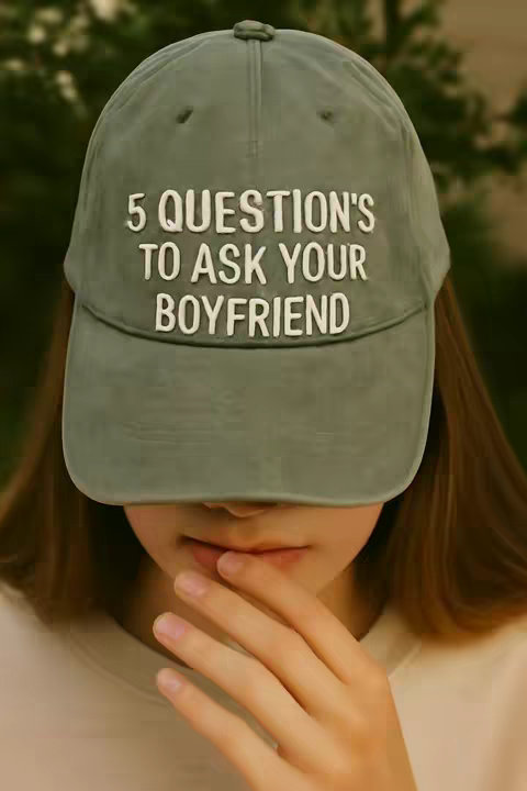 The cover image shows a person, obscured from the nose down, wearing a light green baseball cap. The cap is the focal point and features white, block-lettered text, with the words '5 QUESTION'S TO ASK YOUR BOYFRIEND' arranged across the front. The person's hand is raised and is gently touching their lip. The backdrop appears to be a softly blurred outdoor setting, suggested by the unfocused green hues in the background.