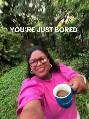 A woman with dark hair and glasses, sticking out her tongue while holding a coffee mug in front of a blurry green background. Text overlayed at the top states 'You're just bored'.