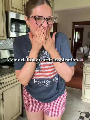 The cover photo features a woman in a kitchen setting, wearing glasses and a graphic T-shirt with an American flag design. She has her hands covering her mouth in a surprised gesture. Text overlayed on the image reads 'Memorial Day Outfit Inspiration.' The background shows kitchen cabinets and a glimpse of another room.