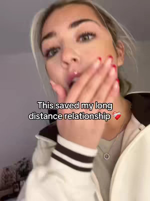 A young woman with blonde hair, wearing a white jacket, is holding her right hand to her left cheek, with a slight open-mouthed expression. Overlayed text reads, 'This saved my long distance relationship.'