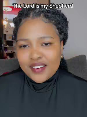 A close-up shot features a woman of color, with dark, curly hair and wearing a black turtleneck. Above her head is a text overlay that reads 'The Lord is my Shepherd' in a white, bold font. The background is blurred, suggesting a domestic setting, and the woman is looking toward the camera with a slight smile.