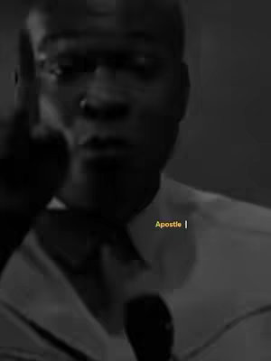 A grayscale image featuring a man with short hair, glasses raising one finger as if making a point. The background is dark, focusing the viewer's attention on the central figure, and the text overlayed is Apostle |