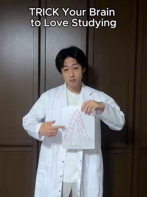 A young man in a white lab coat is centered in the frame, holding a white sheet of paper with a rough, hand-drawn diagram that looks like an A-frame structure with some lines inside, reminiscent of steps. The man is pointing at the drawing with his left hand. Above him, centered, is the text 'TRICK Your Brain to Love Studying'. The background is a plain brown door. The man has dark hair and looks directly at the camera.
