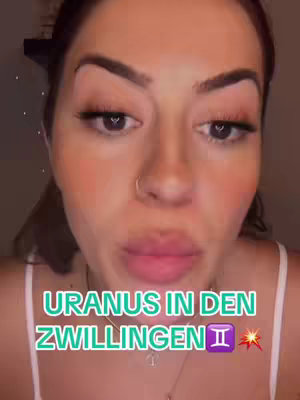 A close-up of a woman with a beauty filter applied, gazing towards the camera. She wears a white top with very thin straps and a necklace. Below the woman, a text overlay reads "URANUS IN DEN ZWILLINGEN" in large, light green letters; the text is positioned over a purple Gemini symbol and a star that is orange.