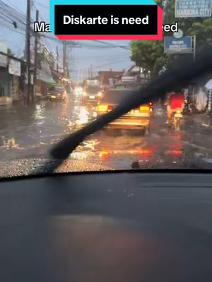 A view from inside a car during heavy rain, with a wiper clearing the windshield. The road is flooded, and cars are visible in the distance. Overlayed text reads "Diskarte is need."