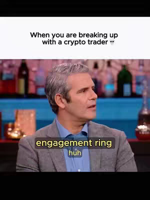 The image is a still from a video featuring a man with short, gray hair, wearing a gray blazer over a blue collared shirt. He's shown from the chest up, with a focused expression and slightly open mouth. Text overlays in a yellow box with black text is placed at the bottom, saying engagement ring and huh. The background appears to be a dimly lit room.