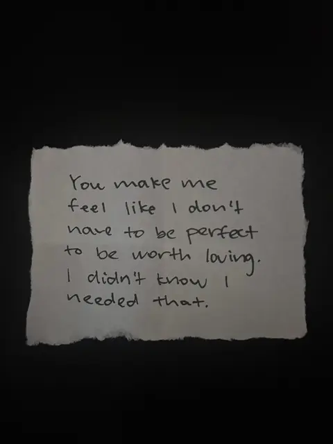 A black background with a piece of torn, textured paper in the center. Handwritten text on the paper reads: “You make me feel like I don’t have to be perfect to be worth loving. I didn’t know I needed that.” The paper has a slightly off-white color, contrasting with the dark background.