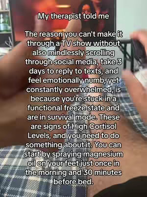 A person's hand holding a phone, with text overlayed on the image. Background appears to be a TV screen and a bed comforter.