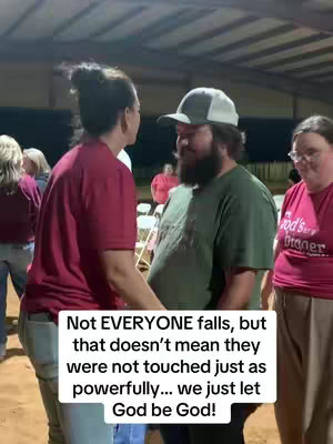 A group of people are gathered outdoors, likely at an event. A woman in a burgundy shirt stands in front of a man with a beard and a baseball cap, seemingly interacting with him. Other individuals, including a woman with glasses, are present in the background. The setting suggests a casual, possibly religious or community-based, gathering.