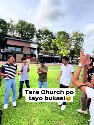 A group of young men are standing on a green lawn in front of a building and trees under an overcast sky. They are in various poses, some clapping or looking at the camera with a text overlay.