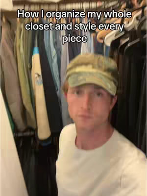 A person standing in front of an open closet filled with clothes. The person is wearing a hat backwards and a white t-shirt.
