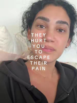 A close-up shot of a woman with dark curly hair. Text overlayed reads: "THEY HURT YOU TO ESCAPE THEIR PAIN". The woman appears to be looking towards the side, with a neutral expression and a slight pout. She is in a dark hoodie.