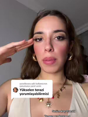 A selfie-style video with a woman in the frame. The woman is looking at the camera and has make-up with an accessory. A text box containing a comment is displayed in the bottom left-hand corner. The main elements are on the woman's face and neck, with a neutral background. The overall lighting is soft, and colors are natural.
