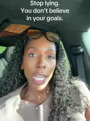 A selfie-style shot features a woman with long, curly dark hair, wearing glasses perched on her head. She is in a car, with the open sunroof visible above. She has her mouth open as if speaking and is wearing jewelry and a light-colored top.