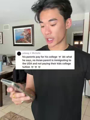 A young man with dark hair and a black t-shirt is holding a phone and looking at the screen. A text overlay in a white box shows a comment from "pdawg Michelle" about parents paying for college, with several emojis. The background is a home setting with a framed picture and other décor.