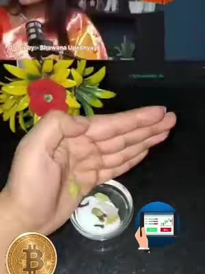 The image shows a woman's hand pouring small green items into a clear bowl. A bitcoin-like gold coin is in the bottom left corner, and a small screen with stock charts is featured in the bottom right. Surrounding the bowl are yellow and red flowers, and a microphone is visible in the background.