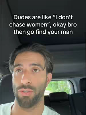 A man with dark hair and a beard is seen from the chest up inside a car. The top of the car interior and a window are visible above him. Text overlayed on the image reads, "Dudes are like 'I don't chase women', okay bro then go find your man."