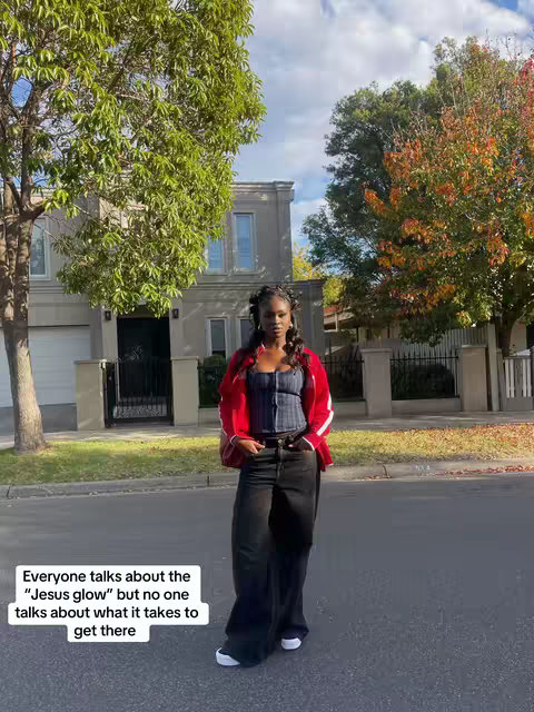 The cover image shows a young Black woman posing on a sidewalk. She's wearing a dark top, wide-legged black pants, and a red jacket. The background includes a house, trees, and a bright sky.