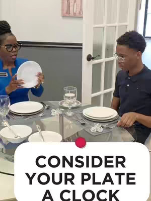 A video cover image shows a woman holding a white plate, instructing a man. A table setting with a plate and silverware is set. Text overlay on the botton states: Consider your plate a clock.