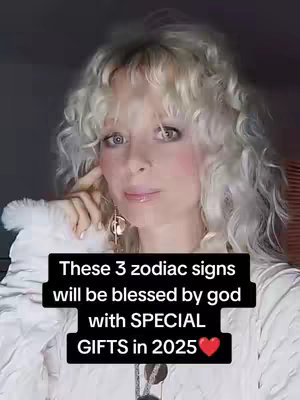 A woman with blonde, curly hair is centered in the frame. She is looking at the camera with a slightly concerned expression. The background is dark. Overlayed across the bottom is a black rectangle with white text that states "These 3 zodiac signs will be blessed by god with SPECIAL GIFTS in 2025❤️"