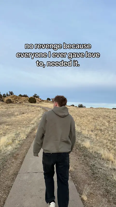The cover image shows a person walking away from the camera on a paved path through a field of dry grass. The sky is overcast. White text saying "no revenge because everyone I ever gave love to, needed it." is overlaid near the top of the image.