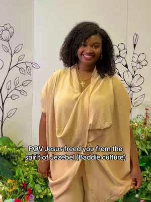 A woman with dark curly hair smiles at the camera, wearing a draped beige outfit and a necklace with a cross pendant against a soft floral backdrop. Text overlaid at the bottom reads "POV Jesus freed you from the spirit of Jezebel (Baddie culture)".
