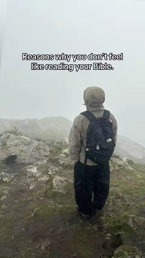 A person wearing a hooded jacket and black pants stands on a rocky hillside, facing away from the camera. The background is a misty, overcast landscape. Text in a white box overlayed on the image reads, "Reasons why you don't feel like reading your Bible."