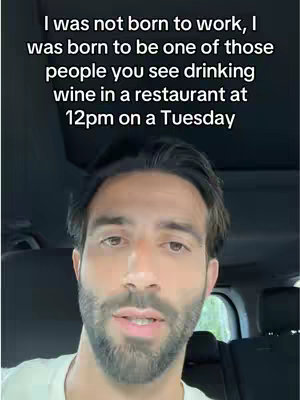 The cover image shows a man in the driver's seat of what appears to be a car. The man is fair-skinned, with dark hair and a neatly trimmed beard. He is looking directly at the camera and speaking. The background is dark and out of focus, but it seems to be a daytime scene. Overlaid on the image is white text containing the following phrase, 'I was not born to work, I was born to be one of those people you see drinking wine in a restaurant at 12pm on a Tuesday'.