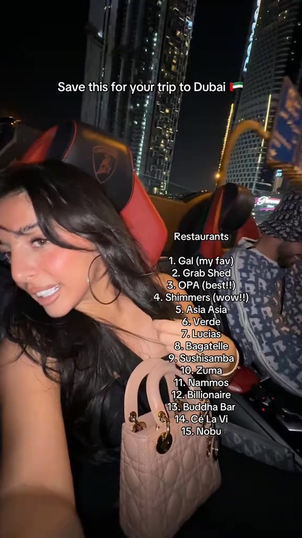 A woman in a car smiles at the camera, holding a pink purse, with a list of Dubai restaurants overlaid on the image. City lights and buildings form the background, creating a nighttime setting.