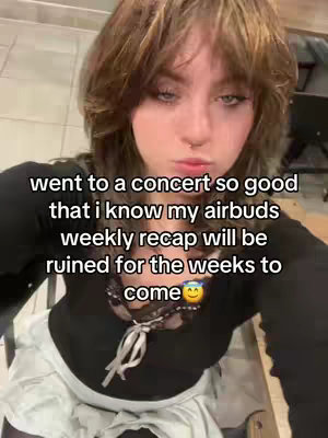 A person with brown hair is shown in a selfie-style video. The person is wearing a black shirt with lace detailing at the neckline and a white skirt. The text overlay reads: "went to a concert so good that i know my airbuds weekly recap will be ruined for the weeks to come".