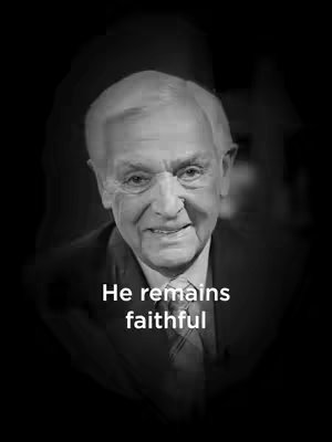 A grayscale portrait focuses on an older man with short, neatly combed white hair and a slight smile. He is set against a blurred dark background, wearing a suit and tie. Text overlayed at the bottom of the image reads 'He remains faithful' in a clean, sans-serif font.