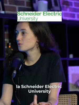 The cover image features a woman seated and speaking into a microphone, with the text "Schneider Electric University" in a green rectangle above her head. Beneath her, at the bottom of the frame, text reads "la Schneider Electric University". The background is dimly lit, and the scene appears to be in a studio setting.