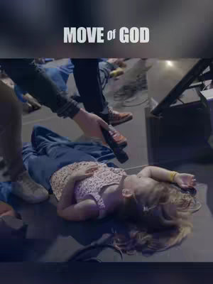The image shows a worship scene with a young girl lying on a reflective floor. People are around her, and someone is holding a microphone. The text 'MOVE of GOD' is overlaid at the top.