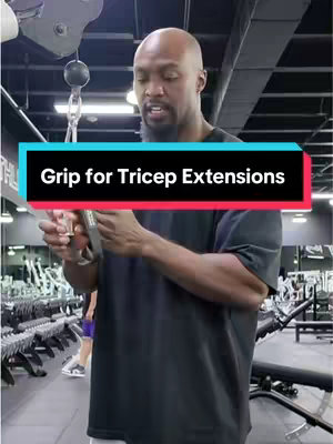 A man in a black t-shirt is holding a tricep exercise cable grip in front of a weight training gym setting with a text overlay at the center-top of the frame.