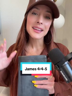 A woman with auburn hair wearing a brown cap is centered, holding a Bible and a microphone. A text box with black and colored text is superimposed on the bible. The background is softly blurred, with some white balloons.