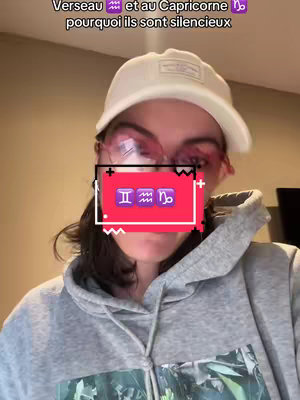 A selfie-style shot of a person wearing a white cap and gray hoodie, pink-tinted glasses, with a red square overlay displaying zodiac symbols. Text at the top reads in French. The background is a plain, light tone.