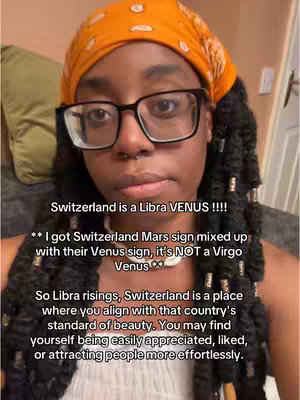 A selfie-style video cover featuring a Black woman with a stylish orange headscarf and glasses. She has long, braided hair adorned with beads. Text overlays are present, with a bold white font over a slightly blurred background.