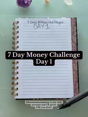 A vertical image shows an open spiral notebook on a light green surface. The notebook has lined pages with a gold spiral spine and a patterned edge. The top of the image has purple and white crystals, and a pen is on the right. Black text overlays on the bottom half of the journal say, "7 Day Money Challenge Day 1."