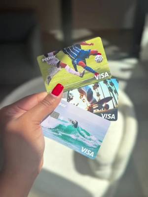 A hand holding up three Pixpay Visa debit cards. The cards display sports and lifestyle imagery. The hand has painted red fingernails, and a light, blurred background is visible.