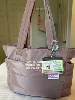 A close-up angled shot showcases a softly lit, dusty rose-colored padded tote bag centered on a white surface. The bag features two shoulder straps, a small tag-like accessory, and a badge. Below the bag, the text overlay reads 'PACK MY BAG FOR A 12 HOUR NIGHT SHIFT (labor & delivery)'. In the background, a light-colored wooden door provides context.